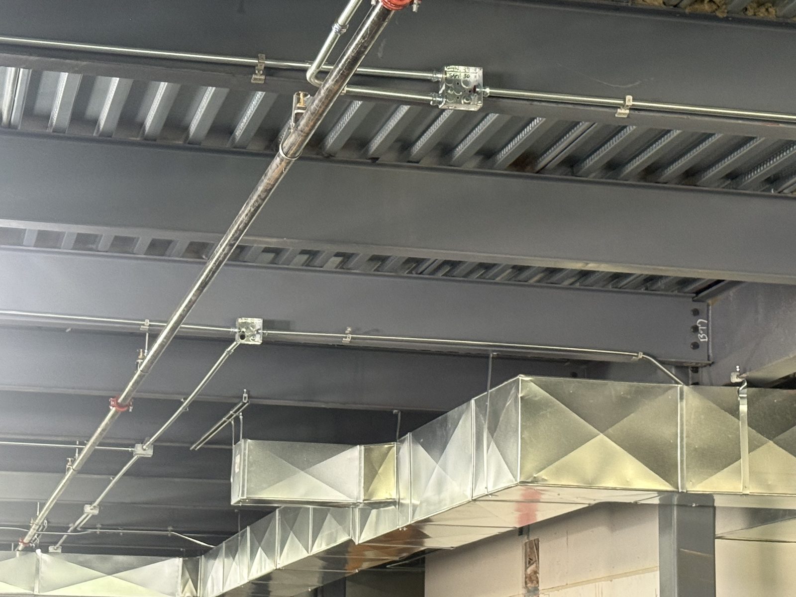 Conduit and junction boxes run along steel beams beside spiral and rectangular ductwork