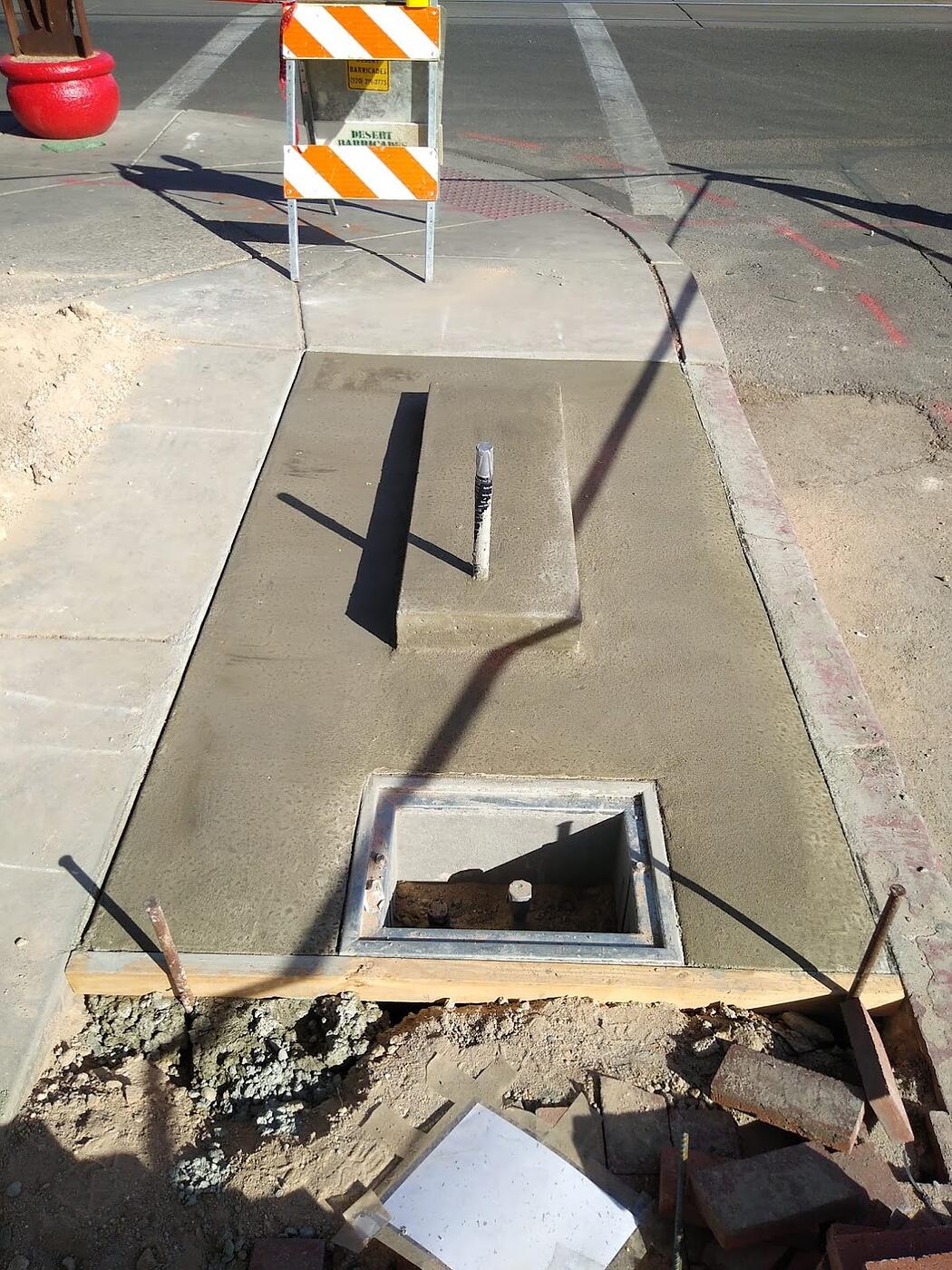 Corner kiosk foundation with conduit stub-up and open pull box next to a curb ramp