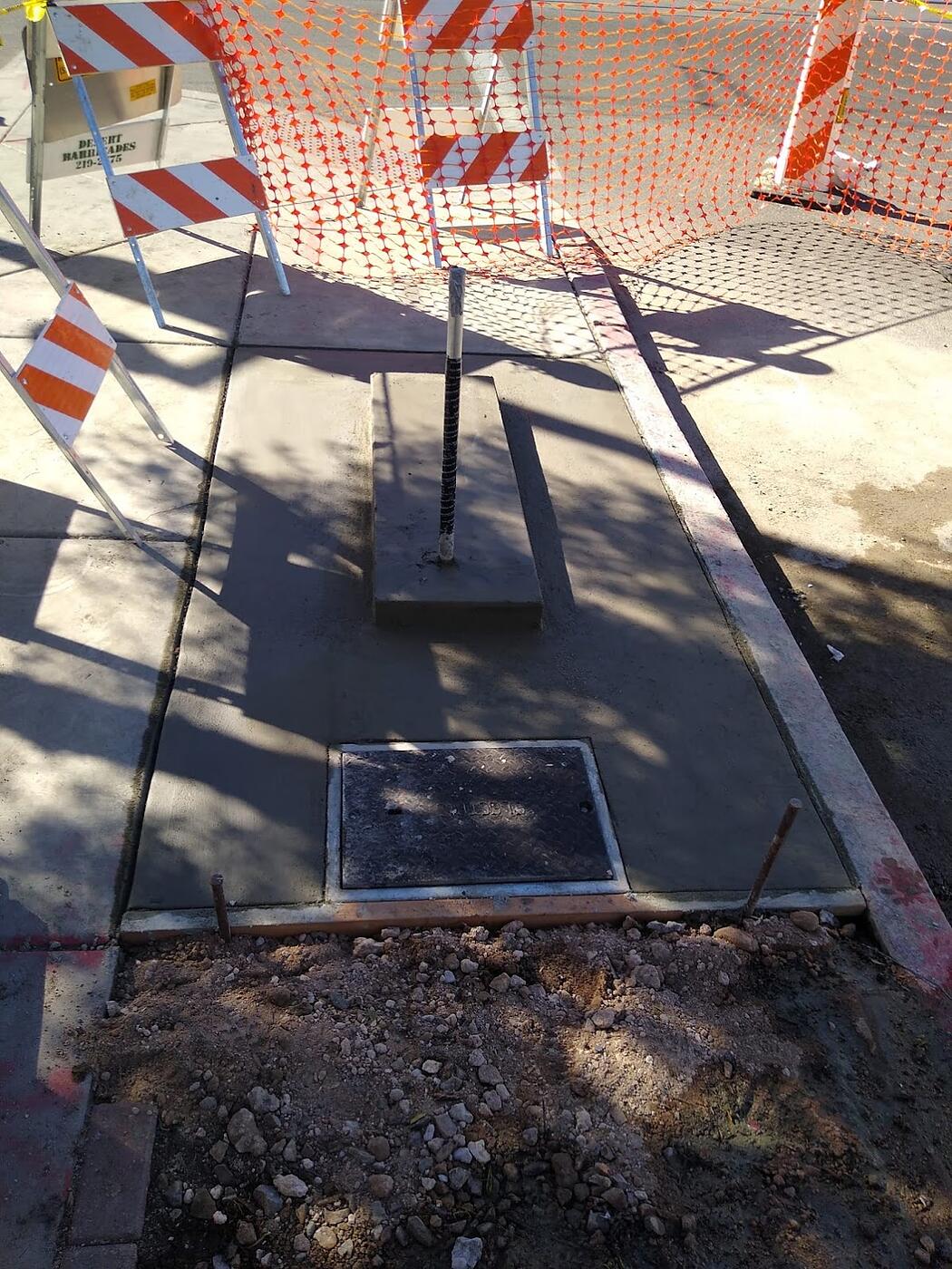 Completed kiosk pad with cast-in pull box lid and conduit stub-up behind construction barricades