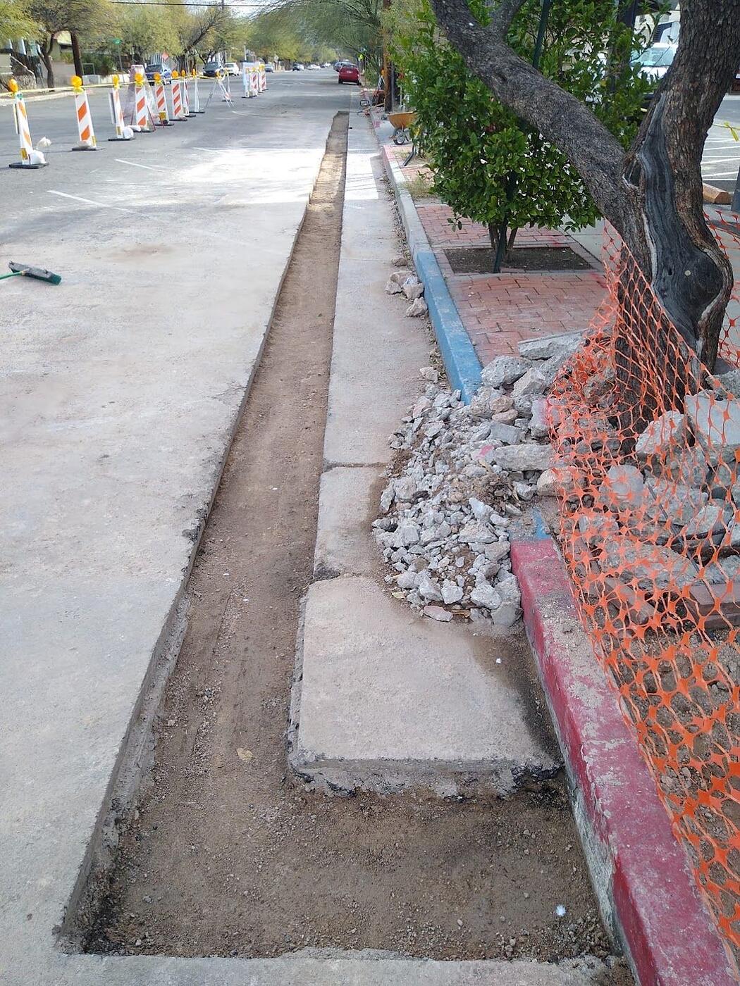 Trench cut along a curb line for kiosk power, sidewalk panels removed and barricades set